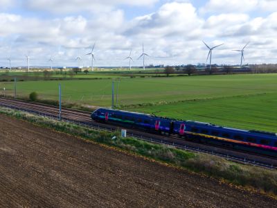 Train travelling past grass field and wind turbines